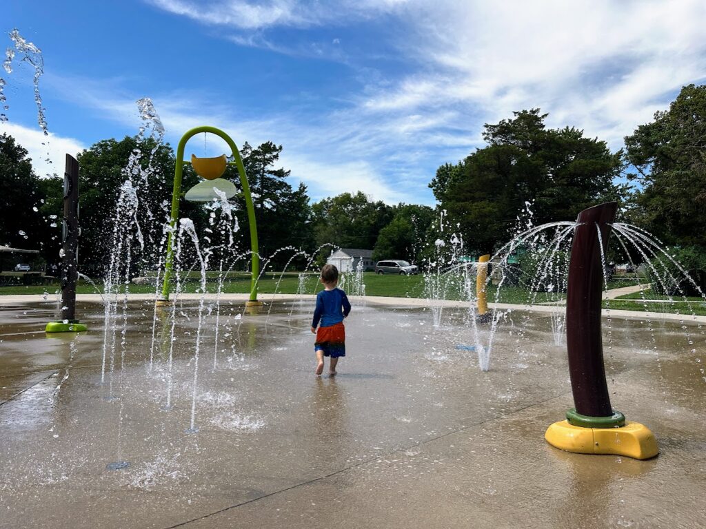 Young child running through fountains at a splash pad on a sunny summer day.