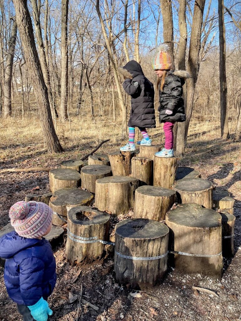 Kids balancing on cut tree stumps in the natural play area at Parkville Nature Sanctuary