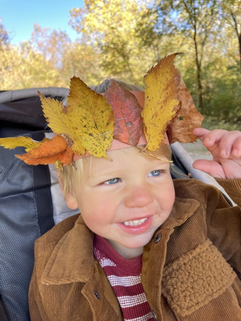 Smiling child wearing a handmade leaf crown during a fall outdoor activity.