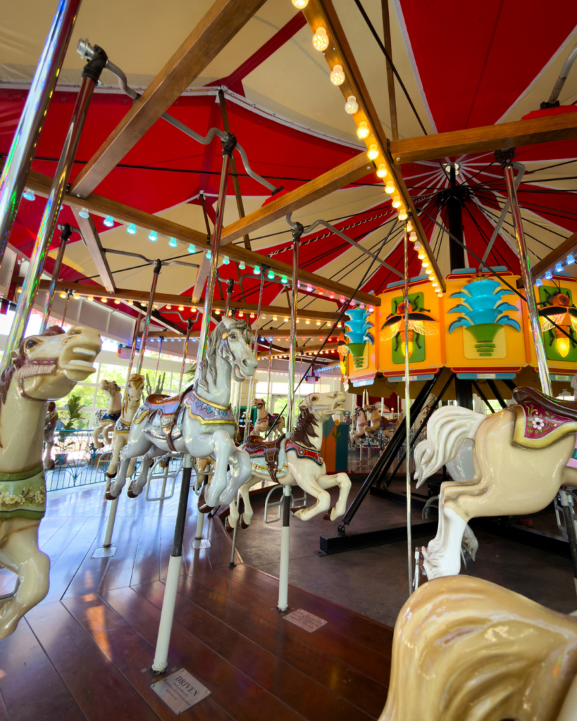 Hand-carved carousel horses circle beneath colorful lights on a beautifully restored carousel at a family attraction in Wichita.