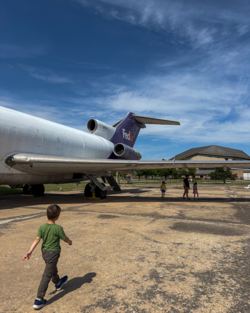 A child explores a retired FedEx aircraft displayed outdoors at an aviation museum, discovering the world of flight and transportation.