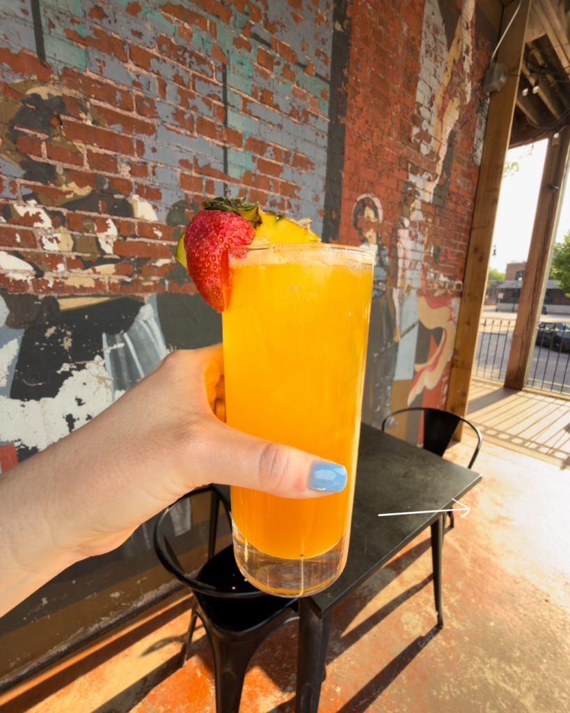 A bright tropical fruit drink garnished with strawberry and pineapple is held up on a sunny patio, creating the perfect summer refreshment.