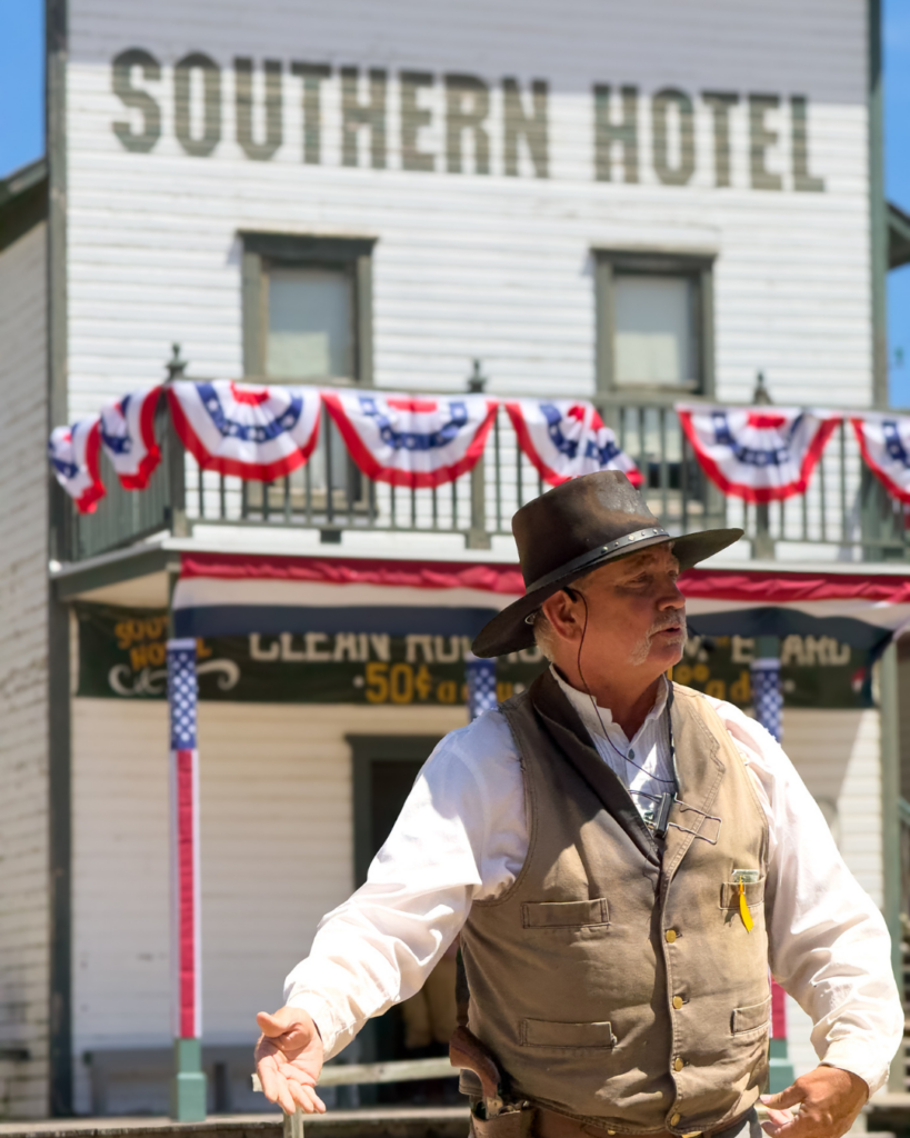 A costumed interpreter shares stories of the Old West in front of the historic Southern Hotel during a living history demonstration.