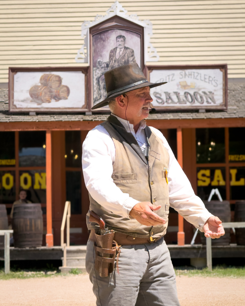 A costumed interpreter shares stories of the Old West in front of the historic Southern Hotel during a living history demonstration.